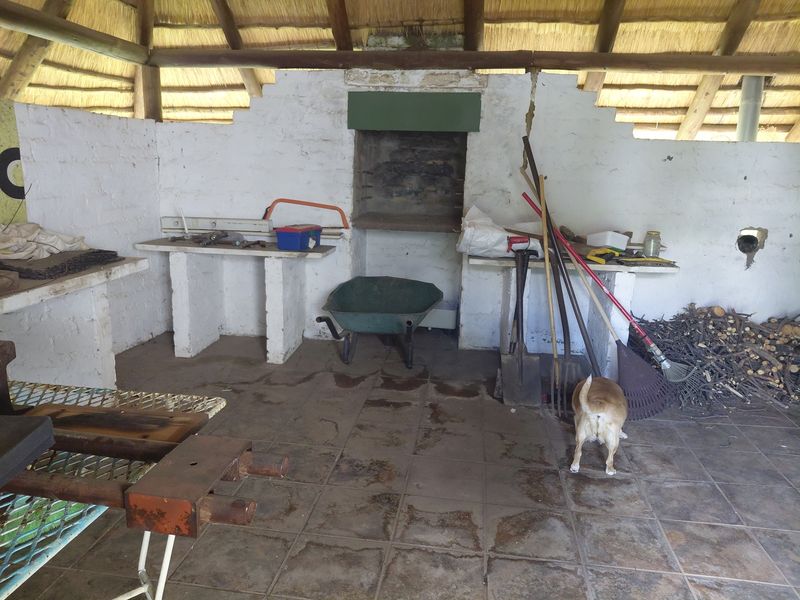 Covered outdoor patio area featuring a thatched roof, tiled flooring, and a built-in braai, offering a functional space for outdoor cooking and entertainment.
