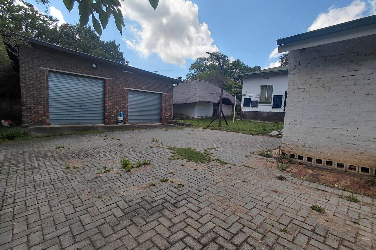 Rear courtyard area featuring a double garage with roller doors, paved driveway, and a secondary thatched structure in a spacious outdoor setting.