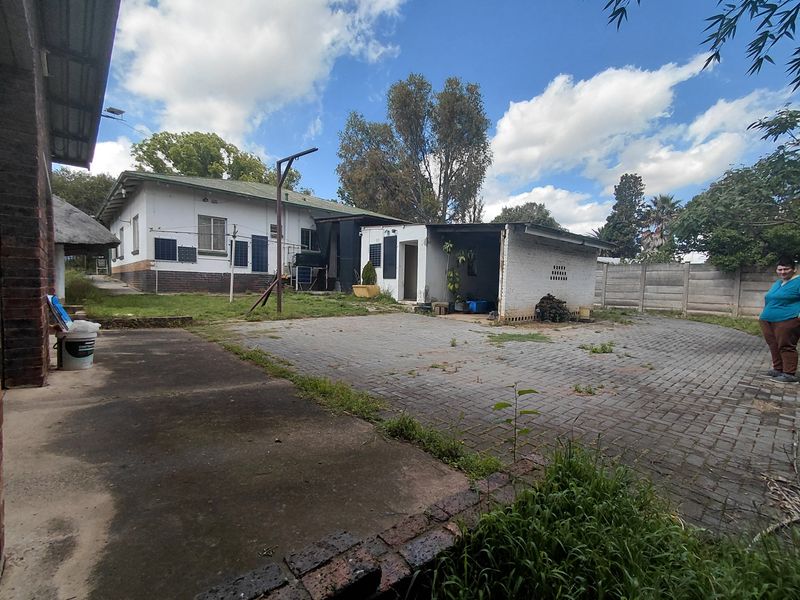 Rear exterior view of the property featuring a paved driveway, concrete patio area, and perimeter precast walling with visible signs of weathering.