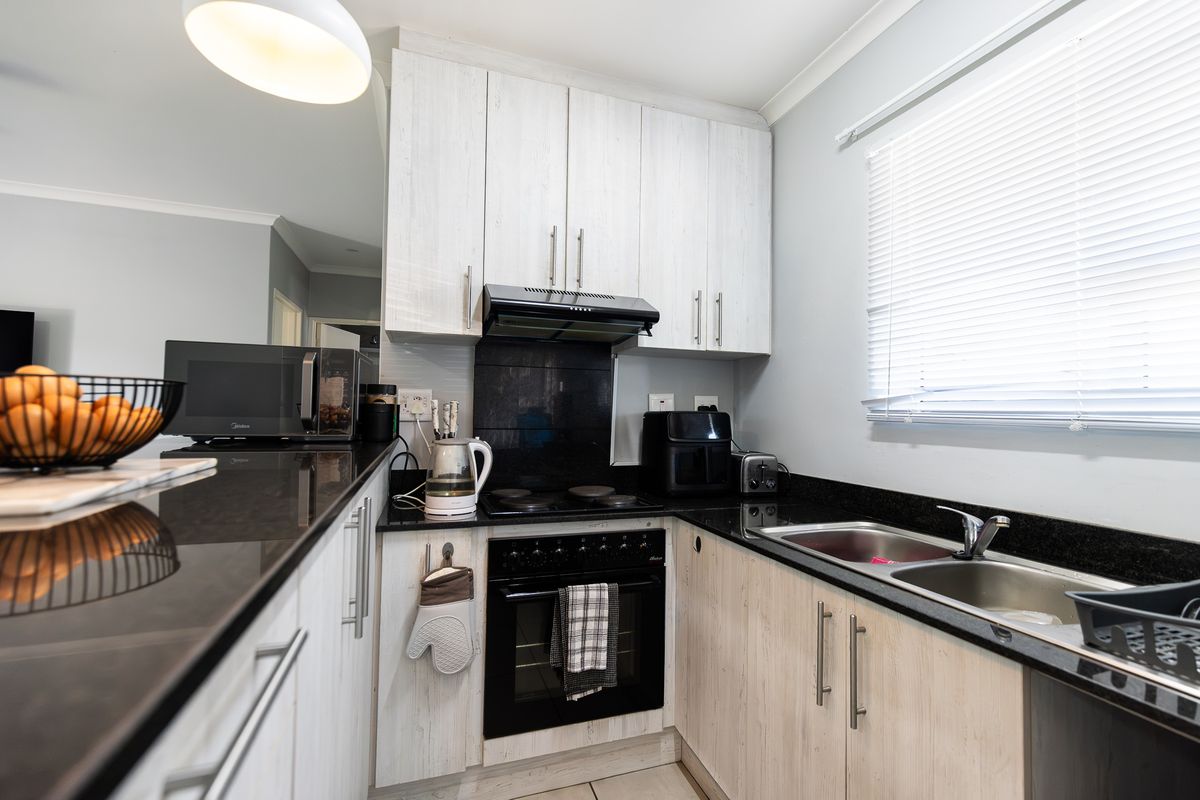A compact, functional kitchen featuring light wood-grain cabinetry, dark granite countertops, a built-in oven with hob, and a double basin sink.
