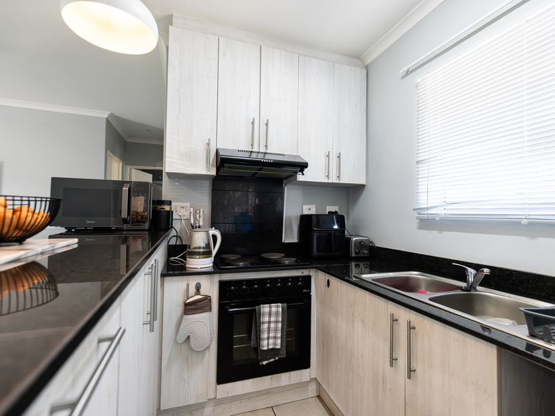 A compact, functional kitchen featuring light wood-grain cabinetry, dark granite countertops, a built-in oven with hob, and a double basin sink.