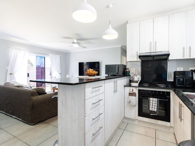 Open-plan kitchen and living area featuring light wood-finish cabinetry, granite countertops, integrated appliances, and direct access to the outdoor space via sliding doors.