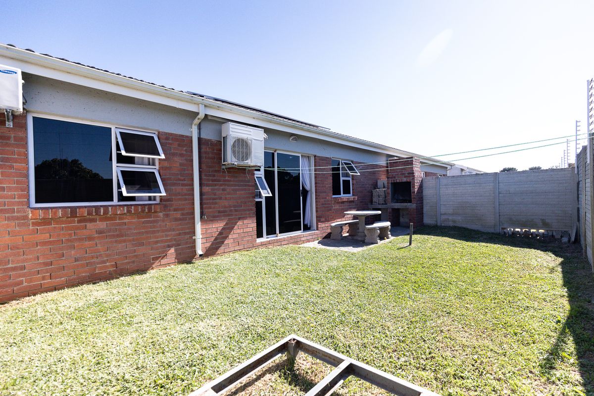 Rear exterior view of the townhouse featuring a brick facade, built-in braai area, sliding door access, and a private garden space.