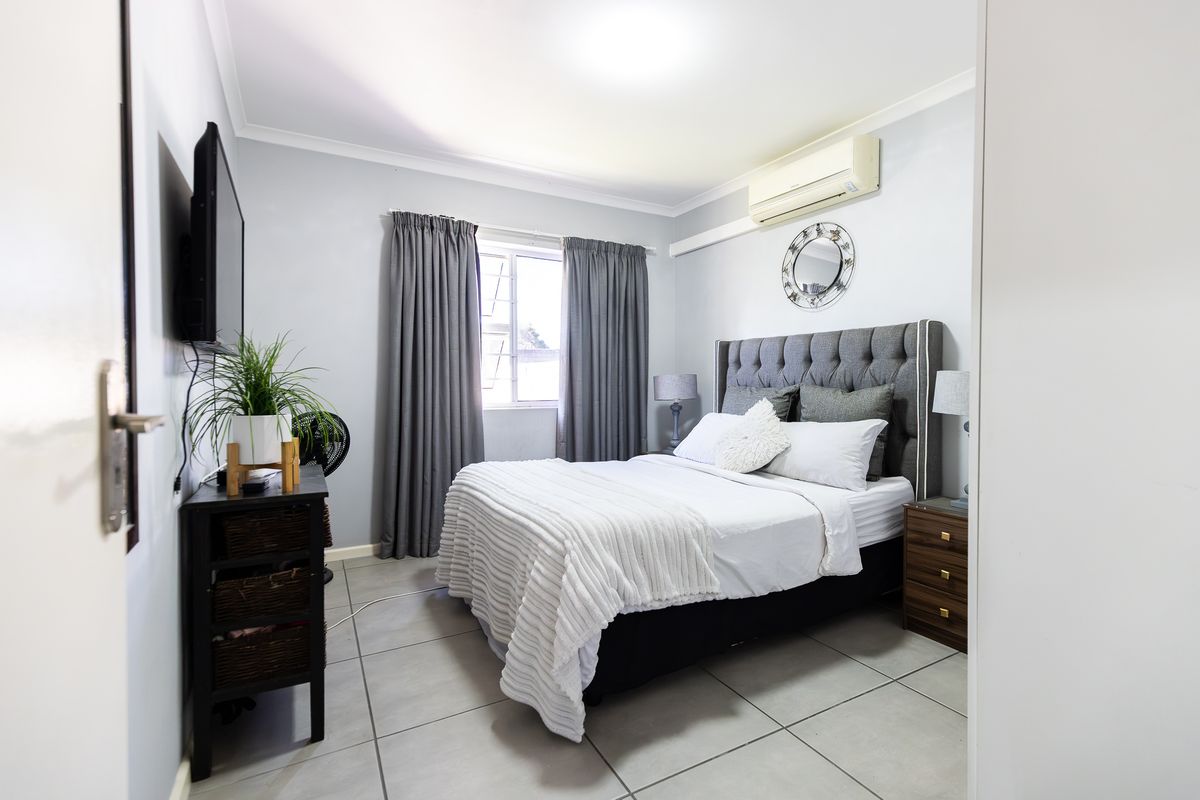 A well-maintained bedroom featuring tiled flooring, a wall-mounted air conditioning unit, and neutral wall finishes.
