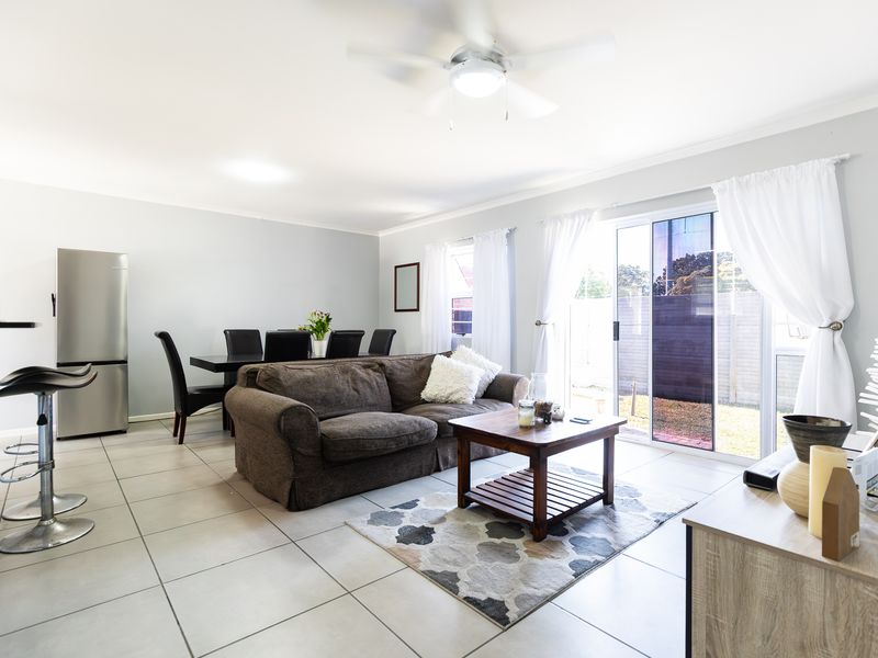 Spacious open-plan living and dining area featuring neutral tiled flooring, a ceiling fan, and large sliding glass doors providing access to the rear garden.