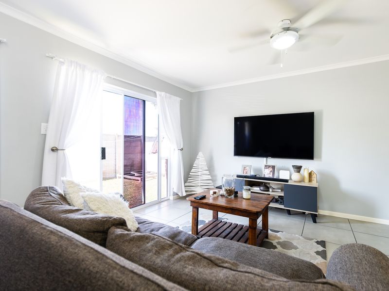 A bright living room featuring tiled flooring, a ceiling fan, and a sliding glass door providing access to the outdoor area.