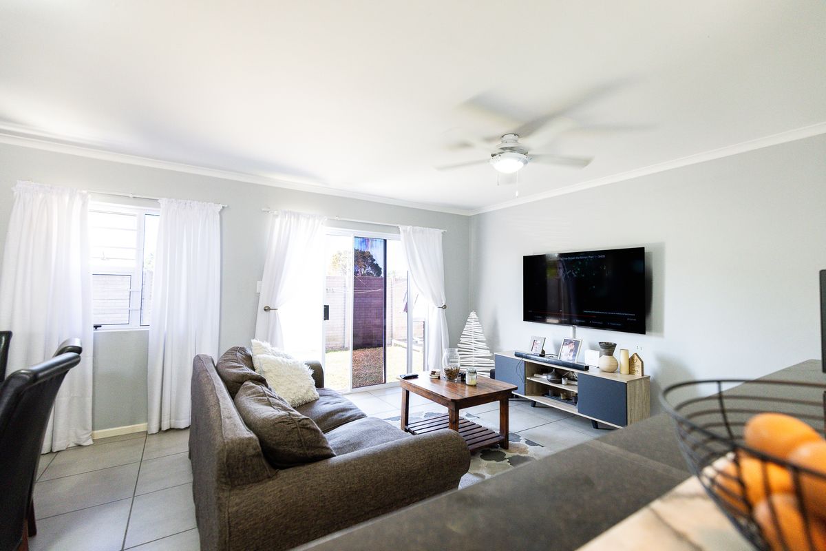 A bright living room featuring tiled flooring, a ceiling fan, and a sliding glass door providing access to the rear outdoor area.