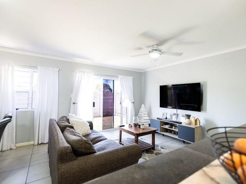 A bright living room featuring tiled flooring, a ceiling fan, and a sliding glass door providing access to the rear outdoor area.
