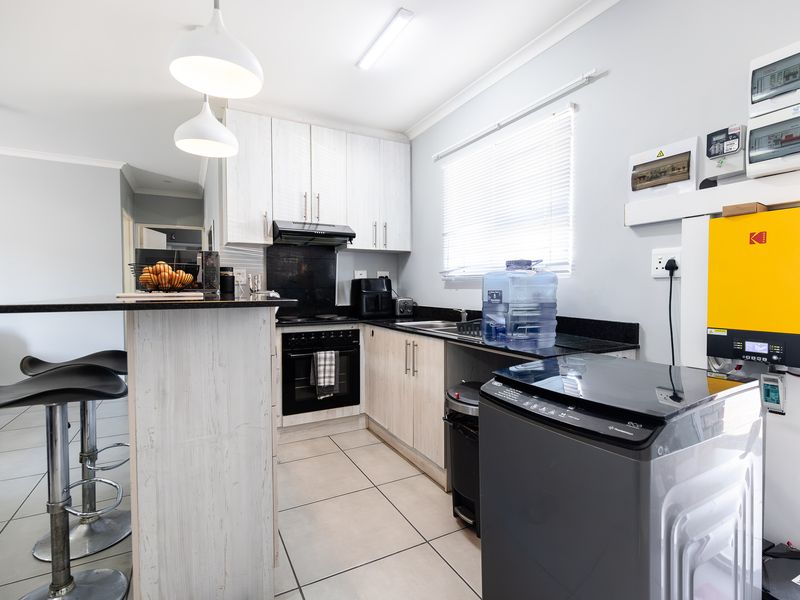 Modern kitchen featuring light wood-grain cabinetry, granite countertops, integrated oven and extractor, and a dedicated solar inverter installation.