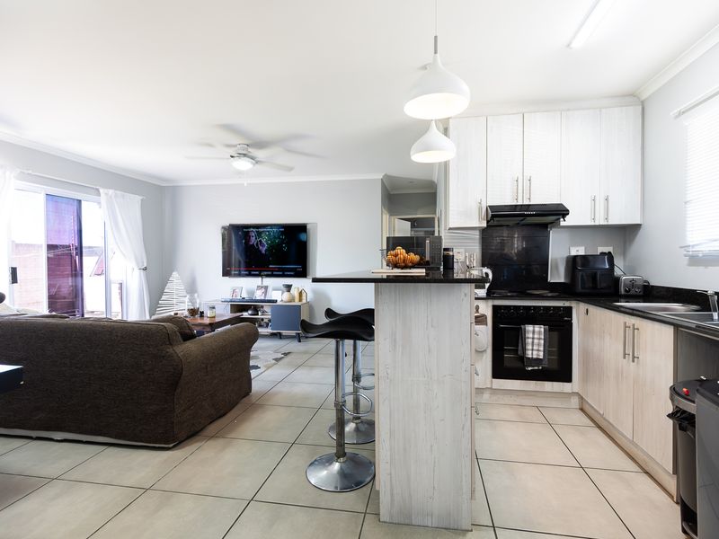 Open-plan living area featuring a modern kitchen with built-in cabinetry, breakfast island, and tiled flooring, seamlessly flowing into the lounge with sliding door access.