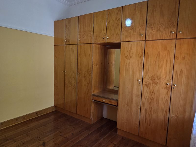 A bedroom featuring extensive built-in wooden cabinetry with an integrated vanity and polished hardwood flooring.
