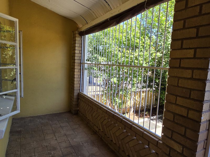A covered outdoor patio area featuring brick pillars, security bars, and tiled flooring, offering a functional space for outdoor relaxation.