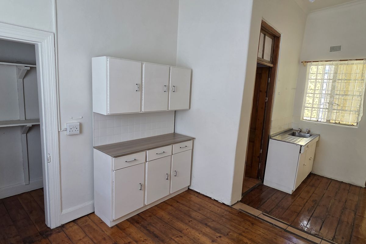 A functional kitchen area featuring timber flooring, built-in cabinetry, a stainless steel sink, and an adjoining walk-in pantry space.