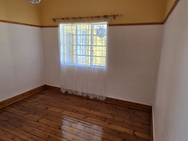 An empty bedroom featuring polished timber flooring, a window with security bars, and traditional picture rails.