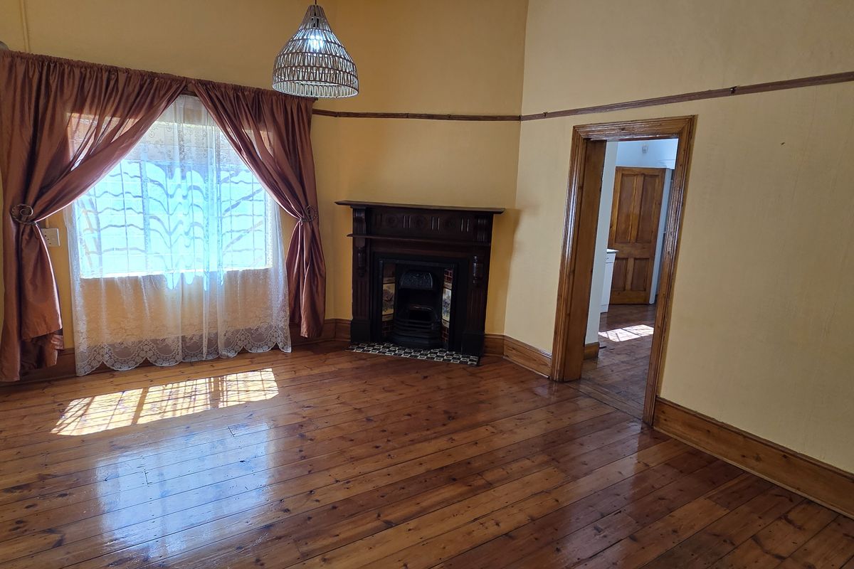 A spacious living room featuring original hardwood flooring, a classic fireplace with a timber mantelpiece, and traditional picture rails.