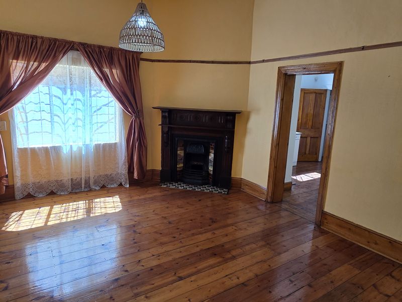 A spacious living room featuring original hardwood flooring, a classic fireplace with a timber mantelpiece, and traditional picture rails.