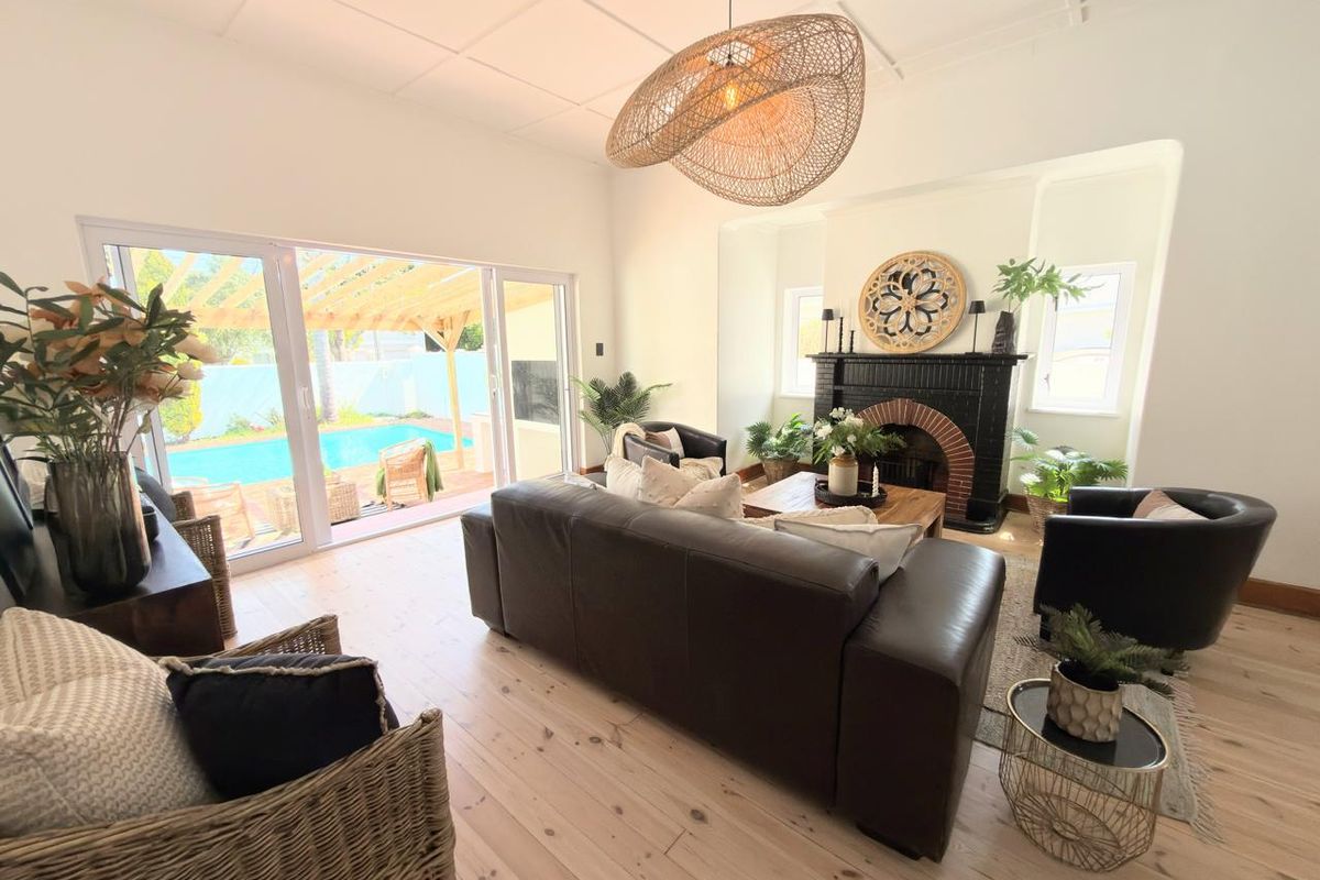Spacious living room featuring a classic fireplace, light timber flooring, and large sliding glass doors providing seamless access to the outdoor pool area.