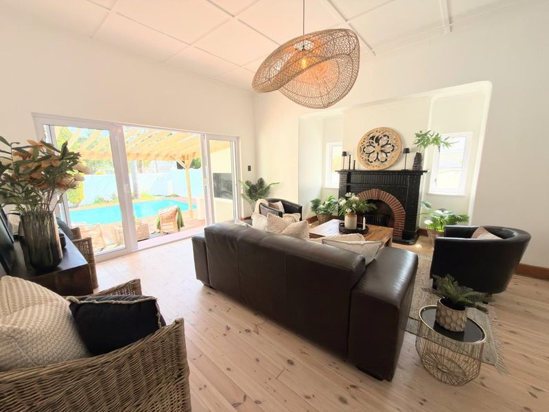 Spacious living room featuring a classic fireplace, light timber flooring, and large sliding glass doors providing seamless access to the outdoor pool area.