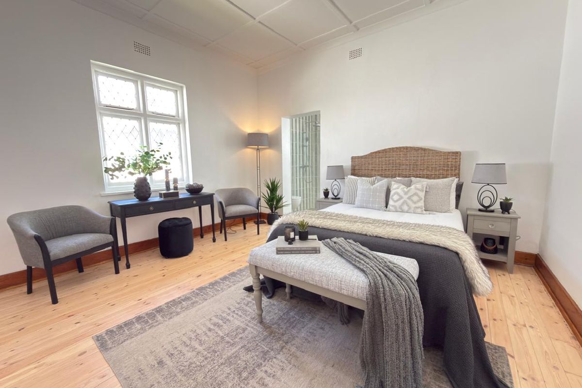 Spacious bedroom featuring polished timber flooring, a decorative coffered ceiling, and leaded glass windows, with convenient access to an en-suite bathroom.