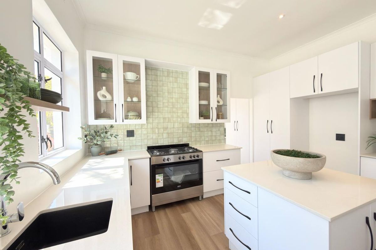 Modern kitchen featuring white cabinetry, quartz countertops, a central island, gas stove, and a stylish tiled backsplash with ample natural light.