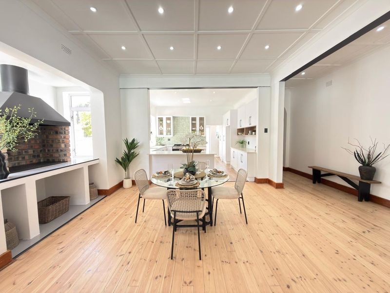 Spacious open-plan living and dining area featuring polished timber floors, a coffered ceiling, and a built-in brick fireplace, flowing into a modern kitchen.