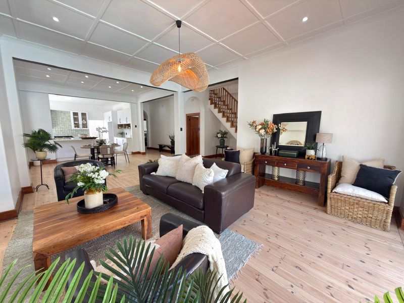 Spacious open-plan living area featuring timber flooring, a coffered ceiling, and a seamless transition to the kitchen, complemented by a central staircase.