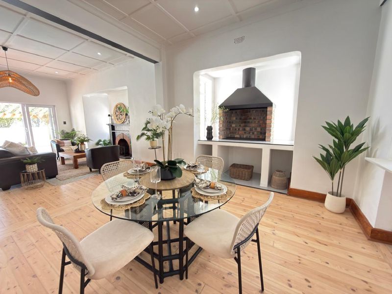 Spacious open-plan living and dining area featuring timber flooring, a coffered ceiling, and a built-in indoor braai with a brick finish.