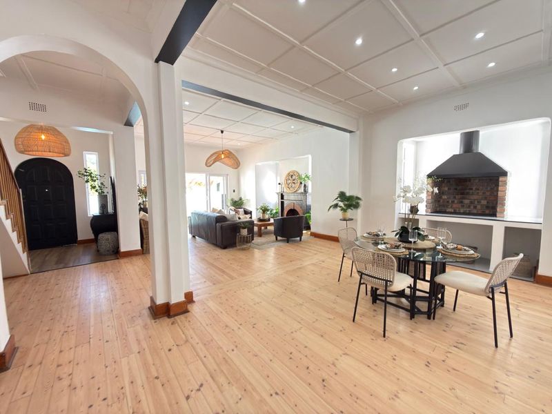 Spacious open-plan living and dining area featuring beautiful hardwood floors, a coffered ceiling with recessed lighting, and a classic built-in brick fireplace.