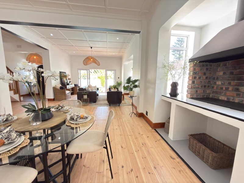 Spacious open-plan living and dining area featuring beautiful timber flooring, a characterful exposed brick fireplace, and a coffered ceiling with abundant natural light.