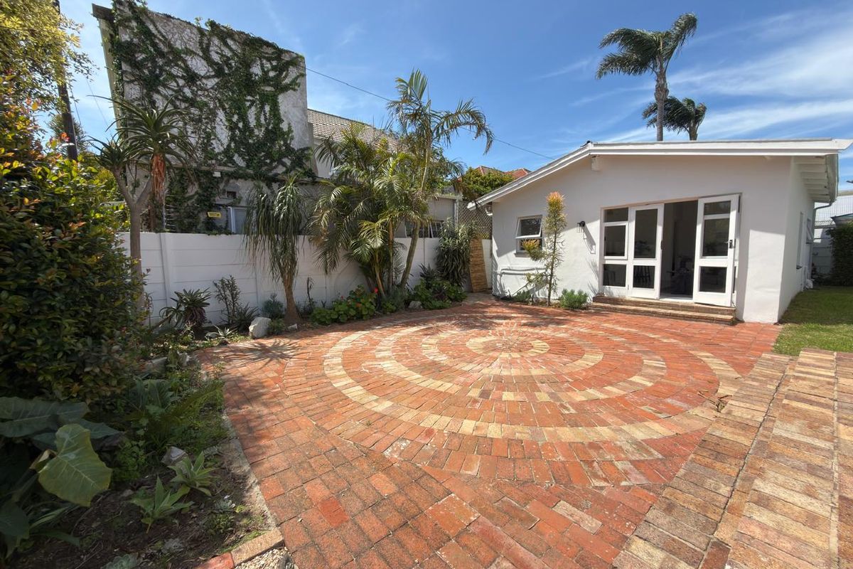 A private rear courtyard featuring a circular brick-paved patio, established garden beds, and direct access to the home through double glass doors.