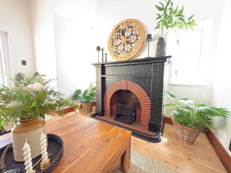 A cozy living room featuring a distinctive black and red brick fireplace as a central focal point, complemented by warm timber flooring.