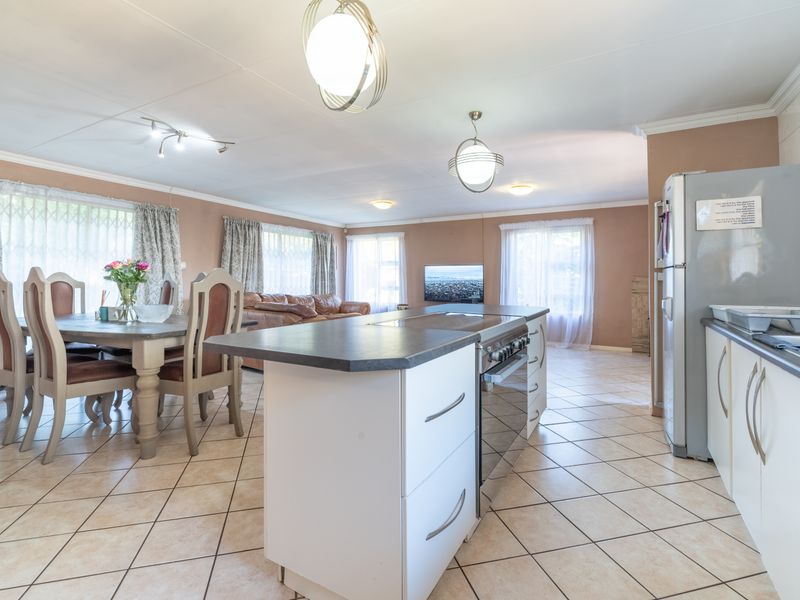 Open-plan living and dining area featuring a central kitchen island with built-in oven and hob, complemented by tiled flooring throughout.