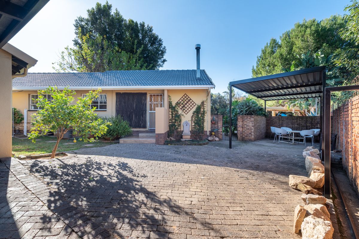 Rear exterior view featuring a paved courtyard, covered patio area, brick boundary walls, and a tiled roof structure with a chimney.