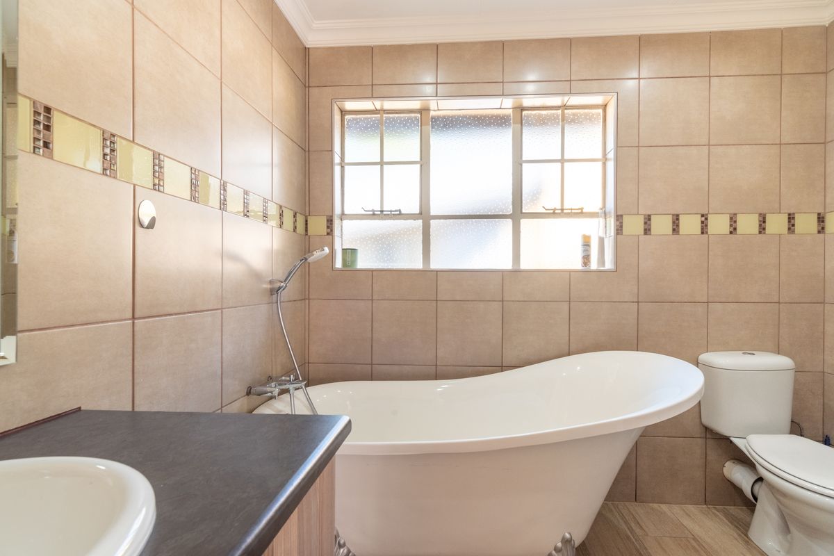 A well-maintained bathroom featuring a modern freestanding bathtub, a vanity with basin, and neutral wall tiling with decorative accents.