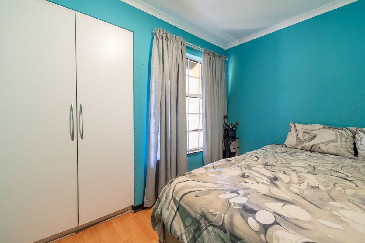 A bedroom featuring laminate flooring, a built-in wardrobe, and a window with curtains, finished with bright blue wall paint.