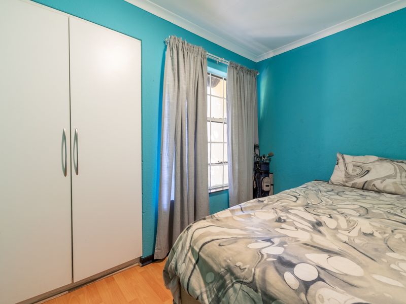 A bedroom featuring laminate flooring, a built-in wardrobe, and a window with curtains, finished with bright blue wall paint.