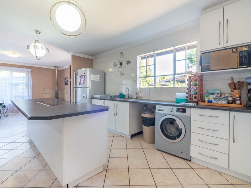 Open-plan kitchen featuring a central island, tiled flooring, ample cabinetry, and integrated appliances, seamlessly flowing into the adjacent living area.