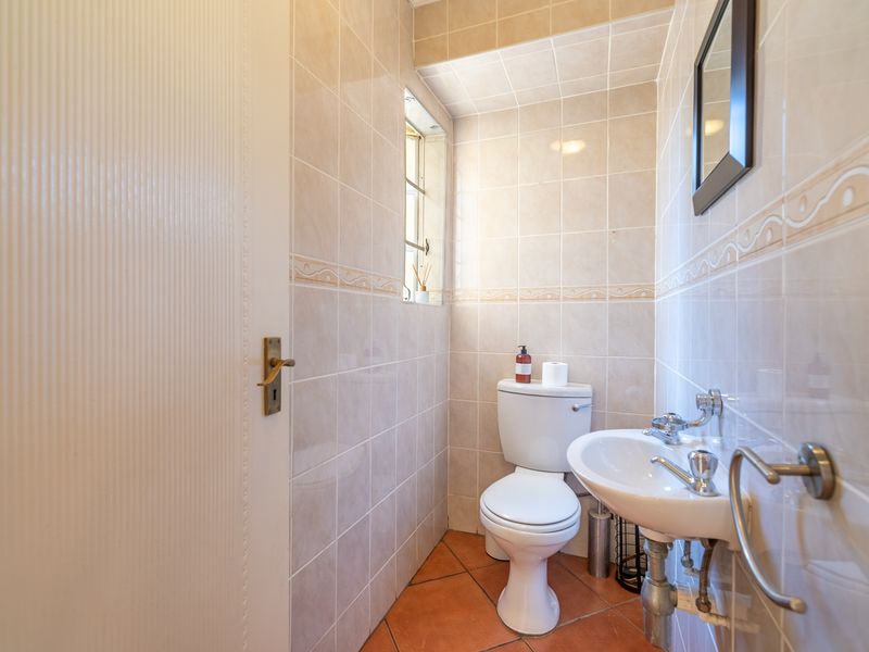 A compact guest bathroom featuring neutral wall tiling, terracotta flooring, a pedestal sink, and a standard toilet.