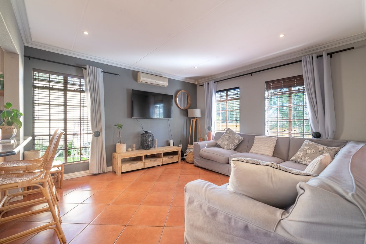 A comfortable living room featuring terracotta floor tiles, split-system air conditioning, and large windows with venetian blinds, creating a bright and inviting space.