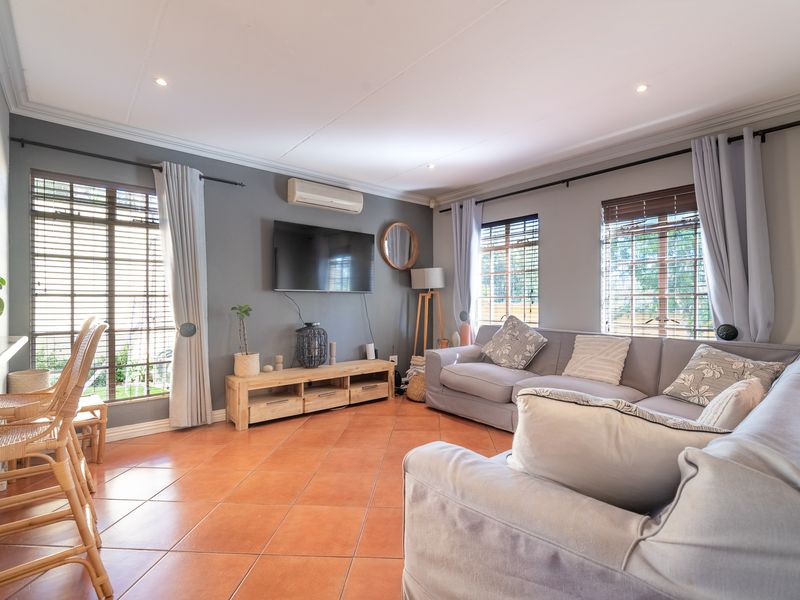 A comfortable living room featuring terracotta floor tiles, split-system air conditioning, and large windows with venetian blinds, creating a bright and inviting space.