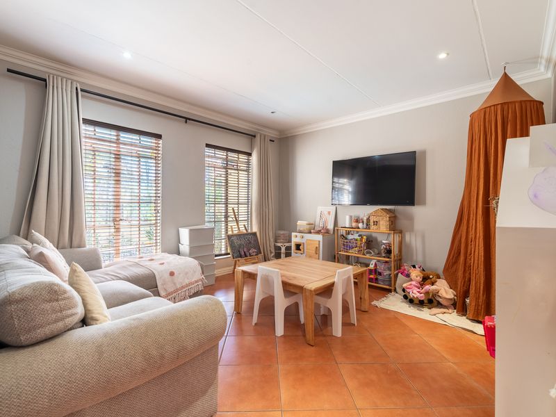 A bright and spacious living area featuring tiled flooring, recessed downlighting, and large windows fitted with venetian blinds and curtain tracks.