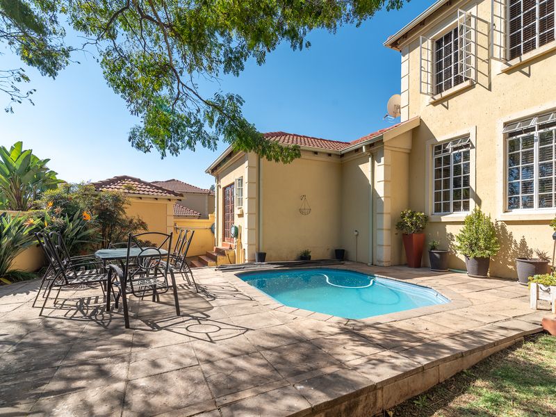 Rear exterior view of the townhouse featuring a private swimming pool, paved patio area, and established garden surroundings.
