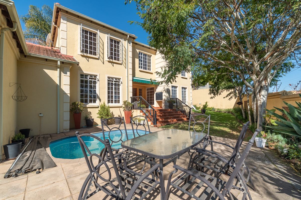 Rear exterior view of the townhouse featuring a paved patio area, a swimming pool, and a landscaped garden with mature trees.