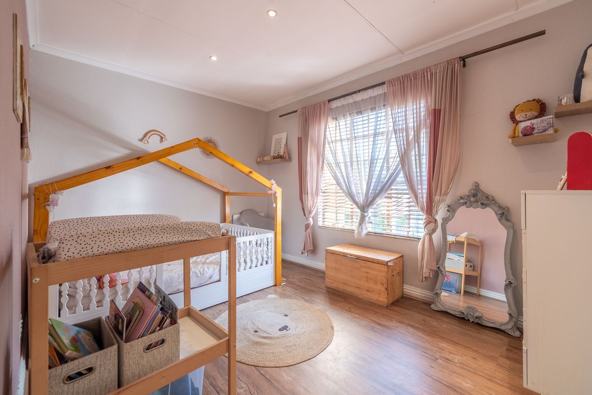 A well-maintained bedroom featuring durable laminate flooring, recessed downlighting, and window treatments including venetian blinds and curtain rods.