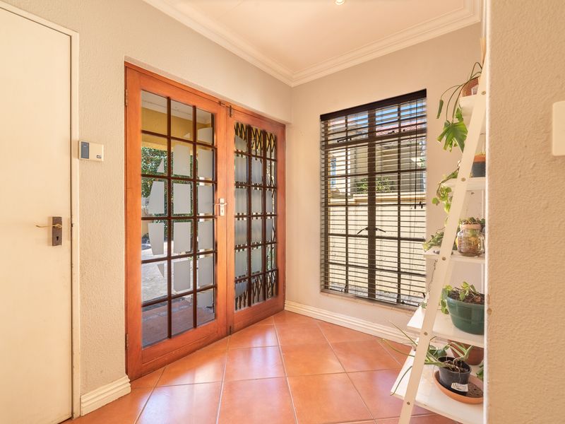 A bright entrance hall featuring tiled flooring, wooden framed glass double doors with security gates, and a window with security bars.