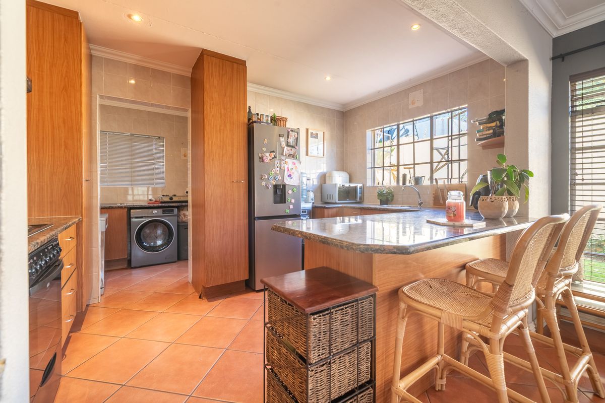 Functional kitchen featuring granite countertops, ample built-in cabinetry, and a breakfast bar, with an adjacent scullery area and tiled flooring throughout.