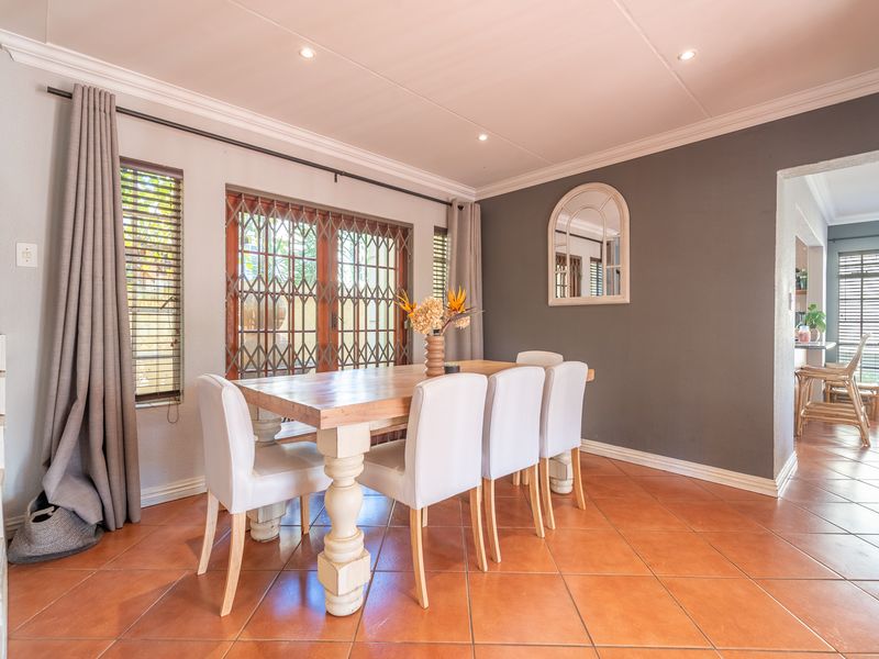 A well-lit dining area featuring tiled flooring, crown molding, and a sliding door with a security gate leading to the exterior.