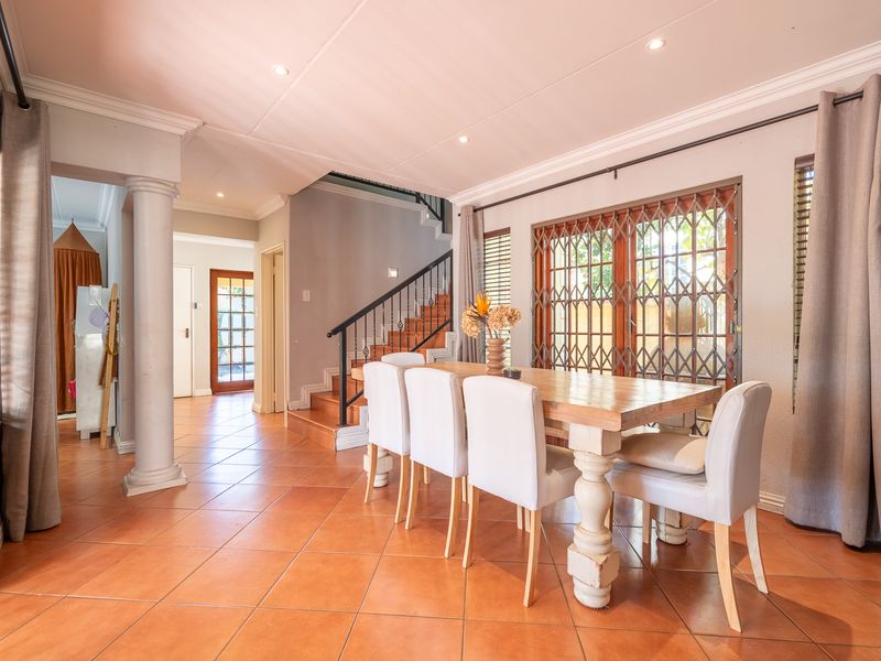 Spacious dining area featuring ceramic tile flooring, a decorative column, and a staircase with a metal balustrade, leading to an outdoor access point.