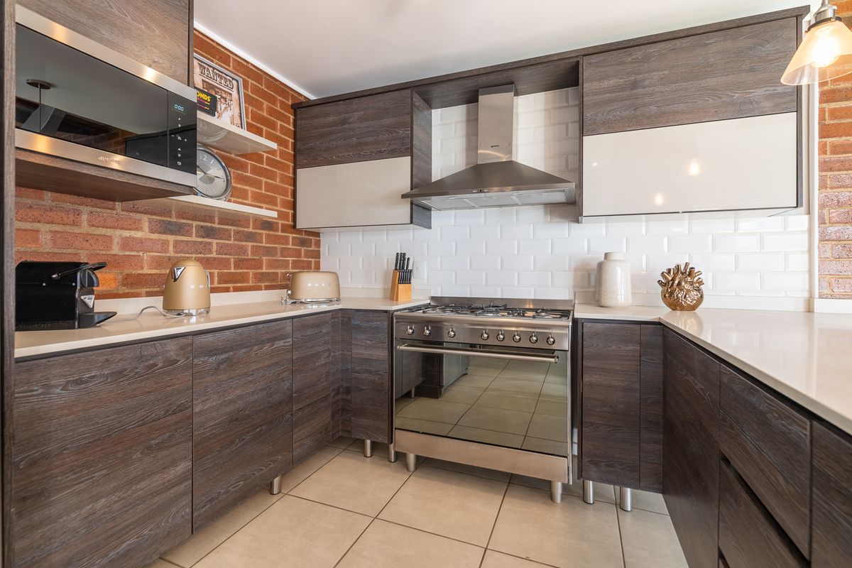 Modern kitchen featuring dark wood cabinetry, stone countertops, subway tile backsplash, exposed brick wall, and high-quality stainless steel appliances.
