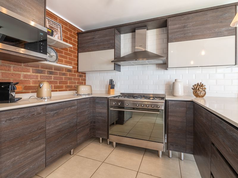 Modern kitchen featuring dark wood cabinetry, stone countertops, subway tile backsplash, exposed brick wall, and high-quality stainless steel appliances.